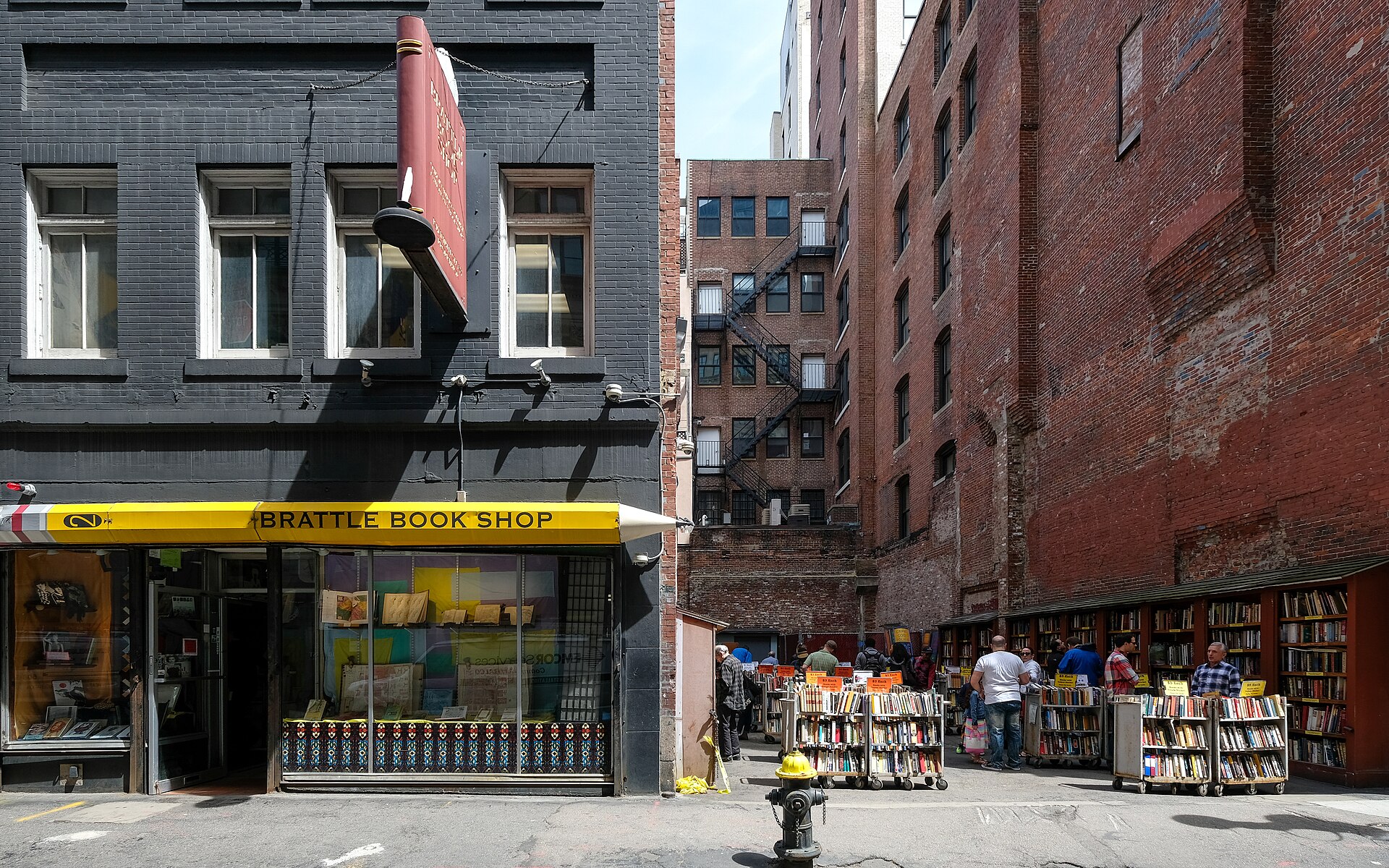 Brattle Book Shop's storefront with browsers at carts of books in the outdoor lot beside it
