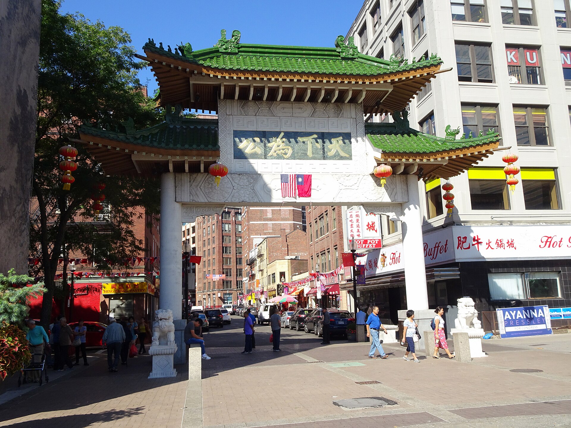 The green-tiled, white stone Chinatown Gate in Boston with shops and pedestrians beyond it