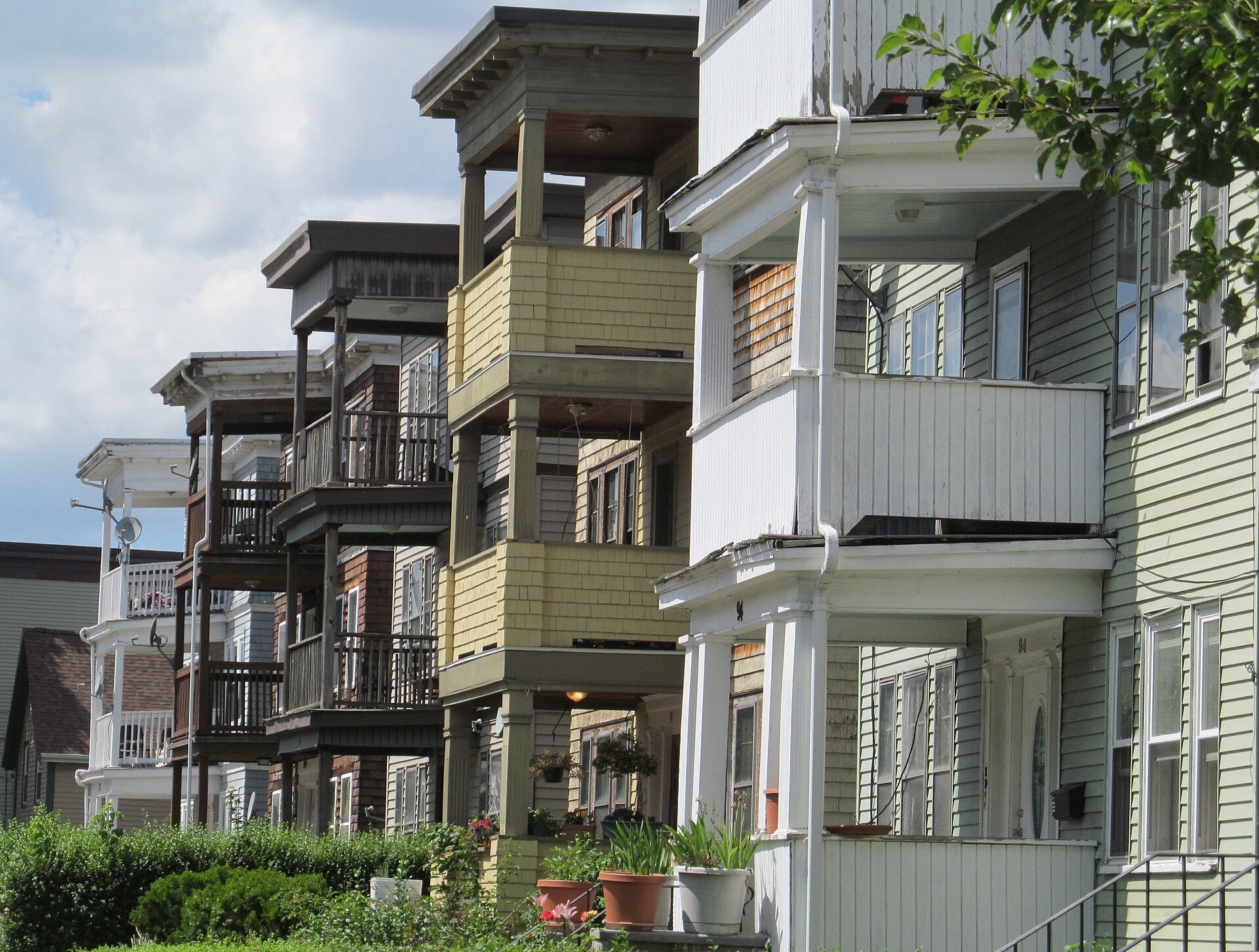A row of wooden triple-decker houses with stacked front porches on a Dorchester street