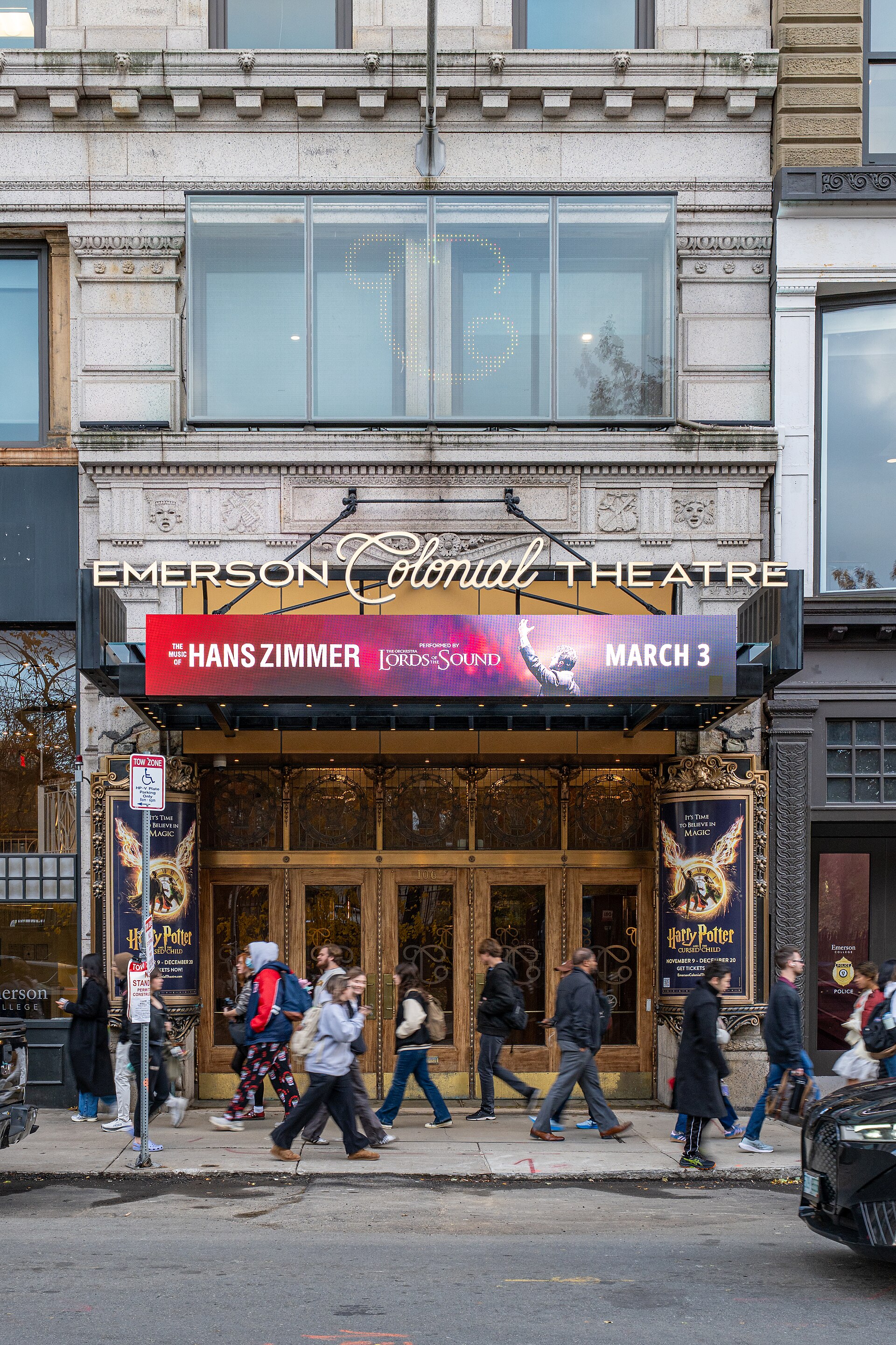 Pedestrians passing the marquee and gilded doors of the Emerson Colonial Theatre