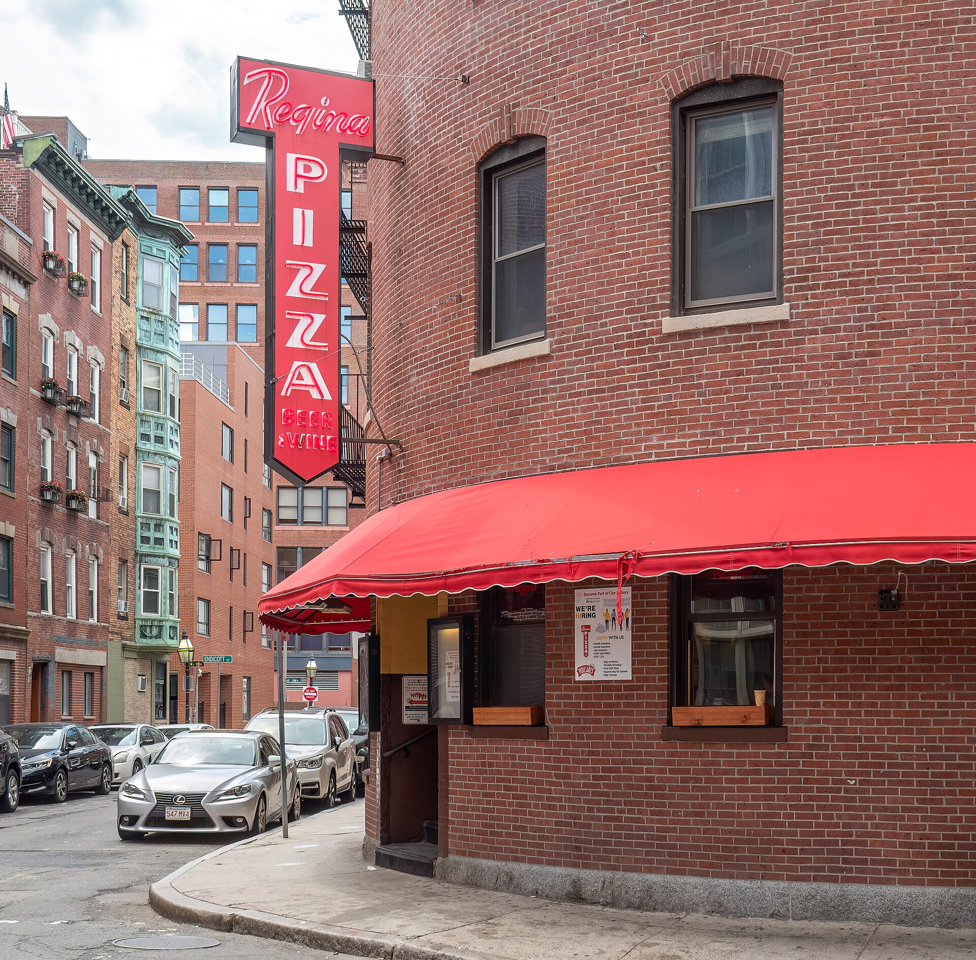 Red awning and vertical neon Regina Pizza sign on a brick corner building in the North End