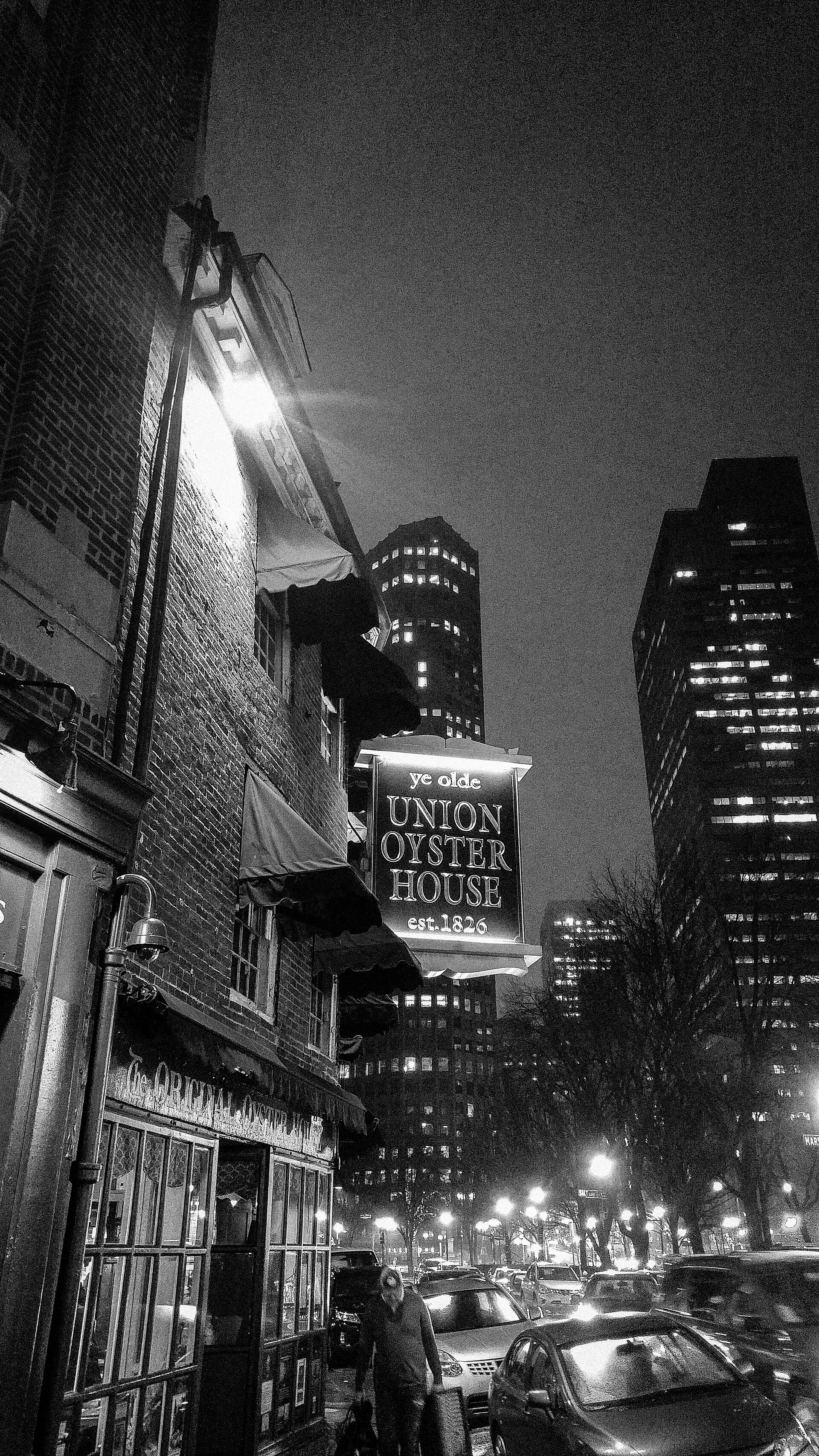 Black-and-white night view of the Union Oyster House's hanging sign and brick facade on Union Street